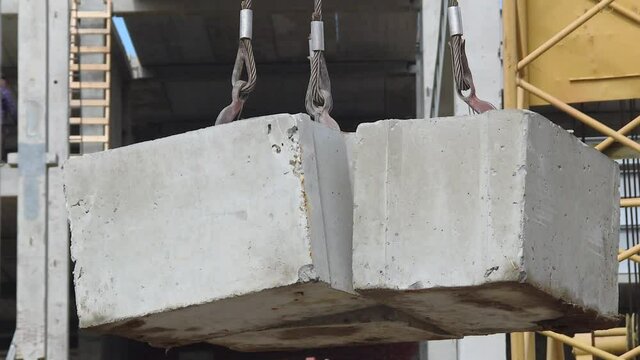 hoisting a concrete slab with crane using metal slings. Concrete slab hanging from crane hook above building skeleton at construction site
