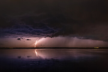 During a night thunderstorm, lightning from stormy clouds hits the ground, and reflected in the...