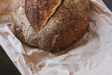 Homemade bread on craft paper on kitchen table. Crispy baked wheat bread surface texture. Selective focus.