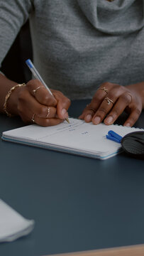 Closeup Of Student With Black Skin Writing Communication Homework On Notebook While Sitting At Desk In Living Room. Young Woman Studying Math On Elearning Platform Doing Homework During High School