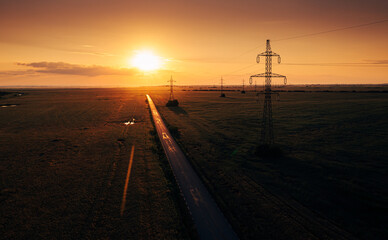 Fototapeta na wymiar Electricity industry. Aerial view of a national electrical power cable line scaffolding during a summer sunrise in the middle of a wheat agriculture field.