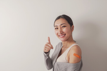 Happy Asian mature woman showing thumb up and her arm with bandage after got vaccinated or...