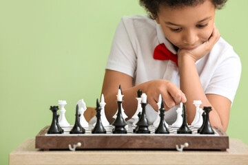 Cute African-American boy playing chess on color background