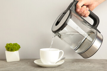 Kettle pouring boiling water into a cup on grey background.