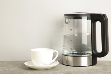 Glass electric kettle with white cup on grey background.