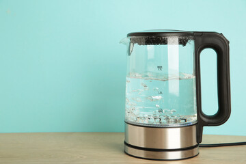 Glass electric kettle with boiling water on blue background.