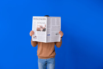 Young man reading newspaper on color background - Powered by Adobe