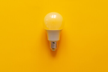 Light bulb on yellow paper background top view