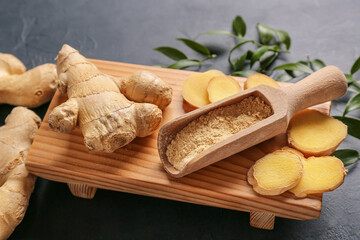 Scoop with ginger powder and roots on dark background
