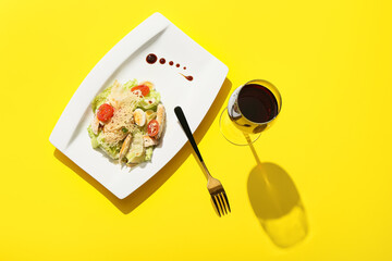 Plate with delicious Caesar salad with glass of wine on color background