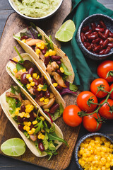 Bowl with tasty guacamole and tacos on dark wooden background