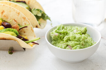Tacos and tasty guacamole in bowl on light background, closeup