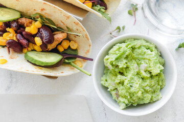 Tacos and tasty guacamole in bowl on light background, closeup