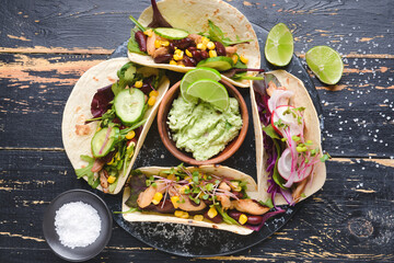 Composition with tacos and tasty guacamole in bowl on dark wooden background