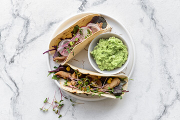 Plate with tacos and tasty guacamole in bowl on light background
