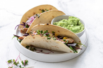 Plate with tacos and tasty guacamole in bowl on light background