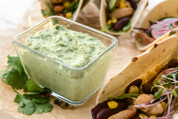 Parchment with tacos and tasty guacamole in bowl, closeup