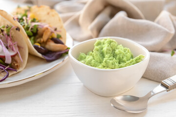 Plate with tacos and tasty guacamole in bowl on light wooden background, closeup