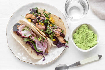 Plate with tacos, tasty guacamole in bowl and glass of water on light wooden background
