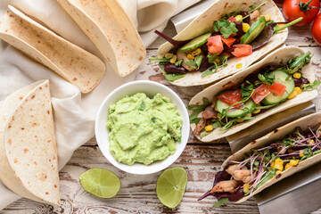 Composition with tacos and tasty guacamole in bowl on light wooden background