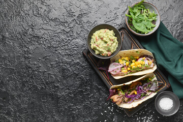 Composition with tacos and tasty guacamole in bowl on dark background