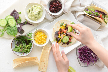 Woman making tasty taco on light background