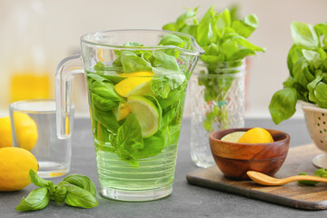 Jug of lemonade with basil on table in kitchen