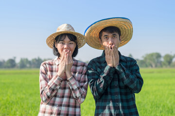 Two Asian farmers standing with wow surprise face at a green rice farm. Couple farmers concept.