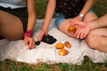 Three unrecognizable friends sitting on the blanket in the park, eating cornbread and reading.
