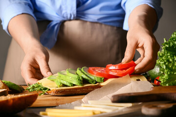 Woman preparing tasty sandwich on table, closeup