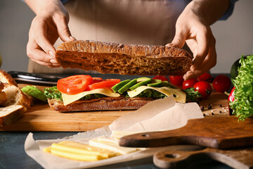 Woman preparing tasty sandwich on table