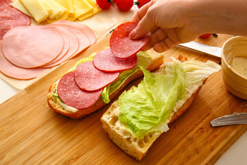 Woman preparing tasty sandwiches on table, closeup