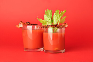Glasses of bloody mary cocktail garnished with bacon and cilantro on color background