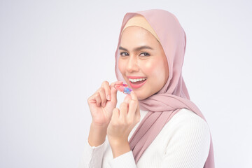 Young muslim woman holding colorful retainer for teeth over white background studio, dental healthcare and Orthodontic concept.