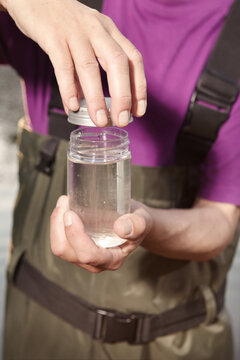 Water quality analyst dressed in chest wader closing bottle with water sample