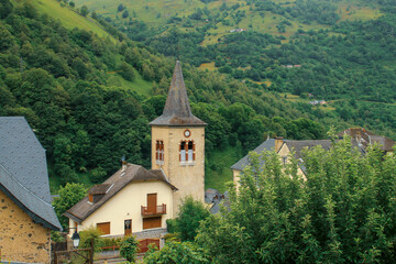 Fotografía de Urdos, pequeño pueblo de montaña rodeado de bosque y nubes en un día lluvioso. Église Sainte-Marie-Madeleine (Iglesia de Santa María Magdalena) en Urdos, Pirineos franceses.