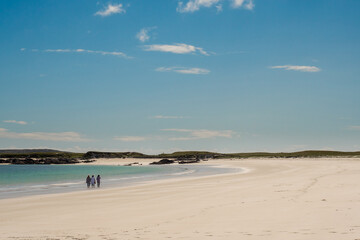 Three women enjoy magnificent Gurteen bay and beach, near Roundstone town, county Galway, Ireland, warm sunny day, cloudy sky. Beautiful Irish landscape, with clear water and light color sand
