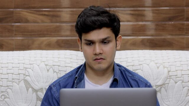 A young college student is disappointed after seeing his semester results on his laptop. Handsome Indian guy is depressed after looking at his exam result on his digital laptop - expressions concept