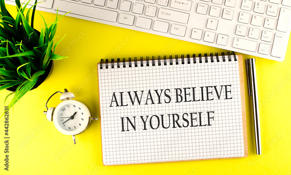 Poster always believe in yourself text on notebook with keyboard , pen and alarm clock on the yellow backgr