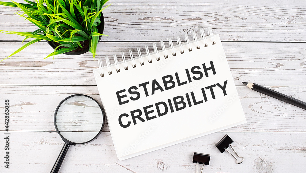 Aufkleber establish credibility text concept write on notebook with office tools on wooden background