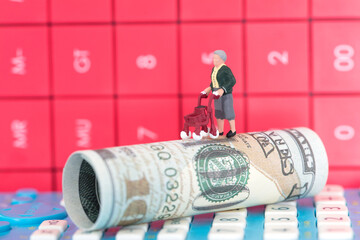 Lonely miniature old man model on dollar bills with calculator background behind