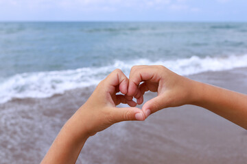 The hands of a young girl show a sign and a symbol of the heart and love for the sea and freedom close-up.