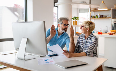 Happy mature business colleagues in modern office using computer and brainstorming.