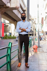 Fototapeta premium Full length shot of handsome black African businessman outdoors in city during summer wearing face mask