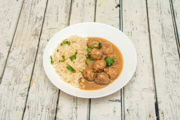 Portion of meatloaf in mushroom sauce garnished with white rice with chopped parsley on a white plate