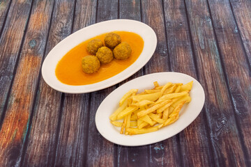 Portion of beef meatloaf in sauce served on a white tray and garnished with hand-cut potatoes fried in olive oil.