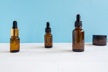 Dark glass and transparent cosmetic bottles with face serum or essentioal oil on a blue background. Unbradned Beauty cosmetic products.