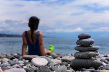 Little girl play with stack stones on the coast of the sea in the nature. Cairn on the ocean beach. Concept of balance and harmony. Calm and spirit.