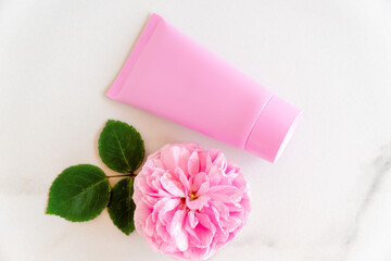 pink tube with rose face or body cream or scrub decorated with pink core flowers. Skin care concept. Unbranding mockup