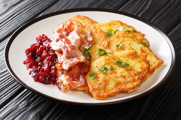 Crispy fried potato pancakes served with lingonberry jam and bacon close-up on a plate on the table. horizontal